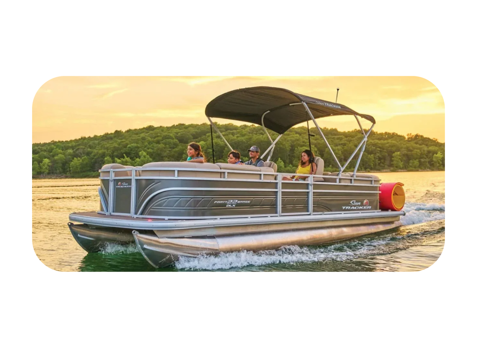 Pontoon boat with people cruising on a lake at sunset, surrounded by trees.