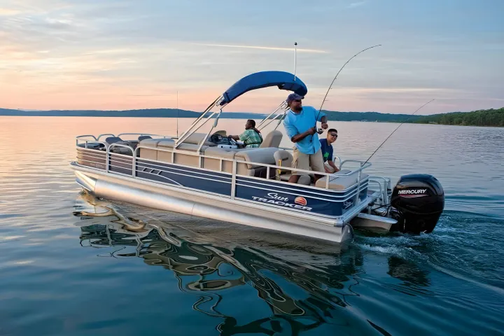 Three people fishing on a pontoon boat at sunset on a lake.